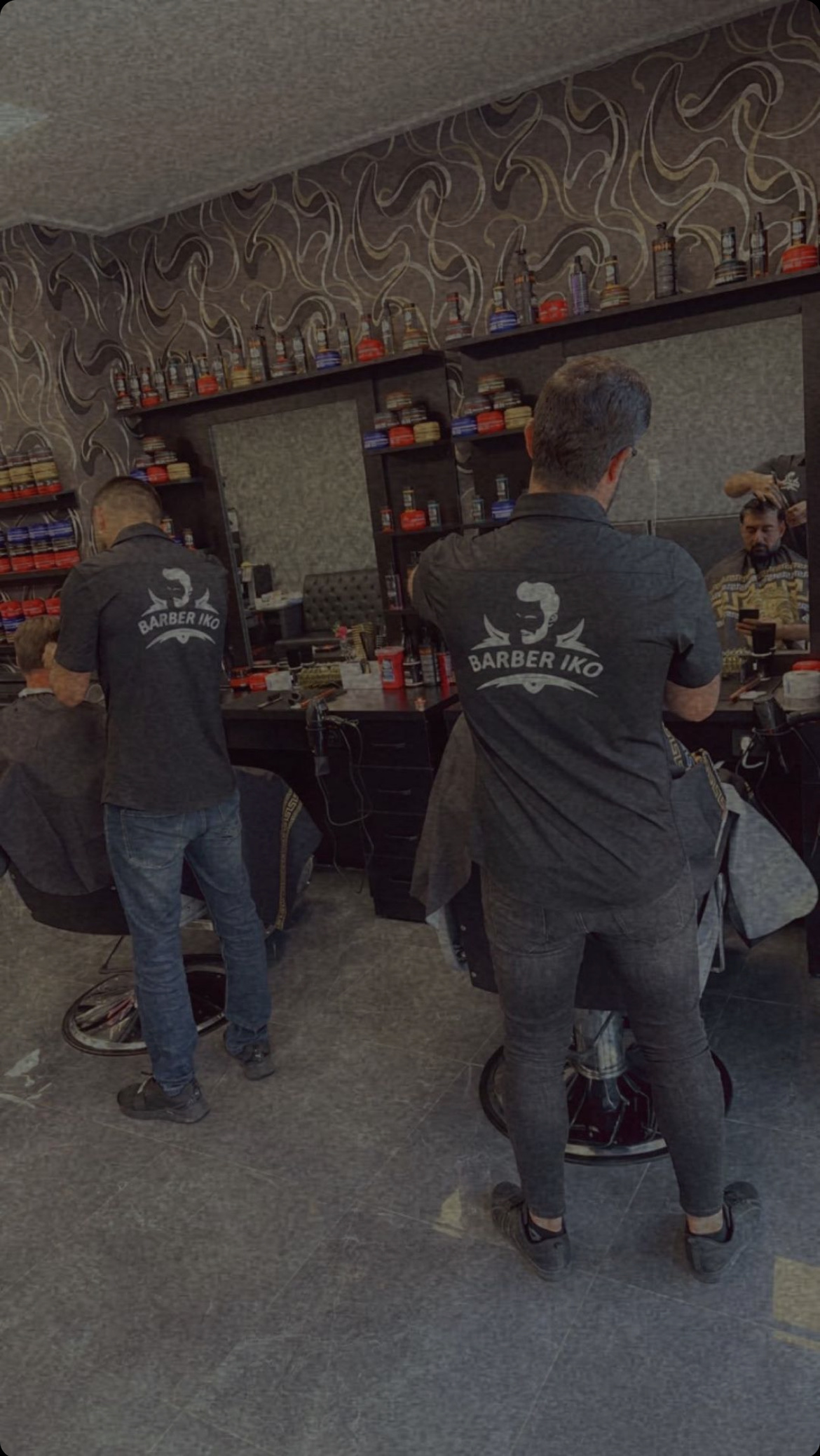 Twee barbers in Barber IKO shirts aan het werk, van achteren gezien